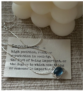Detail of S925 silver necklace with blue oval gemstone pendant on an ivory card