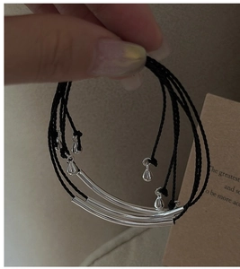 Detail of multi-layered black cord bracelets with silver tubes and water drop pendants