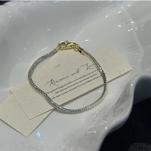 Detail of silver snake chain bracelet with gold lobster clasp on ceramic plate