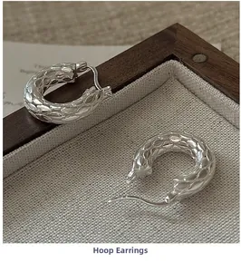 Macro shot of silver hollow S925 earrings with scale texture on a vintage linen tray