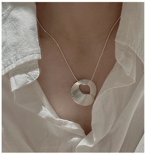 Detail view of S925 sterling silver wavy disc necklace with sleek snake chain on neck