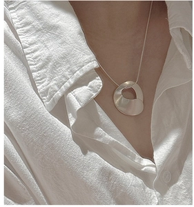Detail of minimalist S925 silver necklace with wavy matte pendant on model neck