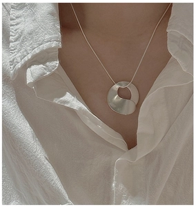 Detail of minimalist S925 silver necklace with irregular matte organic pendant on shirt