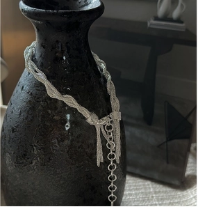 Detailed close-up of woven silver multi-strand snake chain necklace with tassel on a black vase