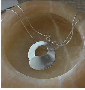 Macro detail of silver irregular geometric pendant with matte brushed finish and snake chain