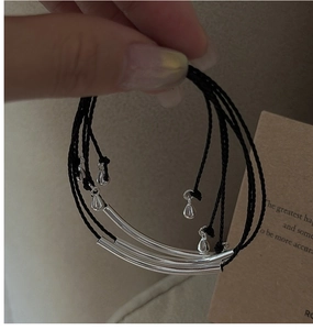 Detailed view of triple-layered minimalist silver bracelets with woven cord and charms
