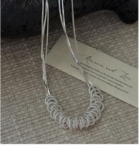 Detail of silver S925 twist rings pendant on a triple strand chain against a soft fabric