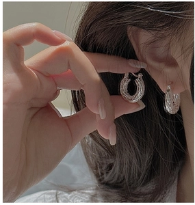 Macro shot of silver 925 hoop earrings with intricate woven texture on a model ear
