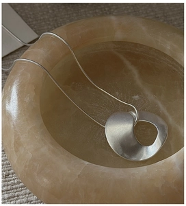 Detail of matte silver twisted ring pendant on sleek snake chain over stone decor