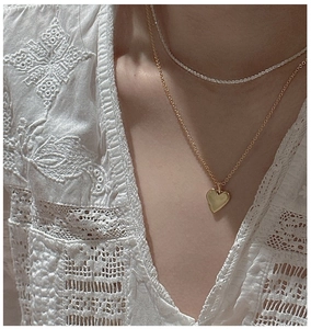 Détail d'un collier pendentif cœur doré et d'un ras-du-cou en perles sur dentelle