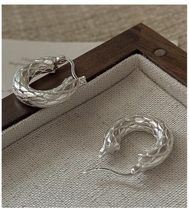 Macro detail of S925 sterling silver hoop earrings with 3D scale texture on fabric