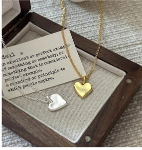 Détail macro de pendentifs cœur en or et argent sur chaînes fines dans un coffret cadeau