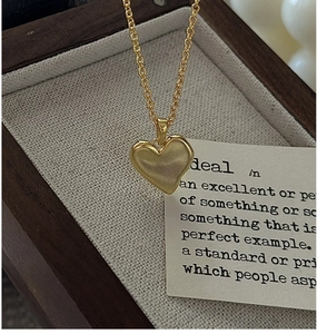 Détail d'un collier pendentif cœur doré mat reposant dans une boîte à bijoux en bois