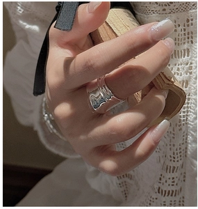 Detailed view of a wide silver band ring with textured wavy design on model hand