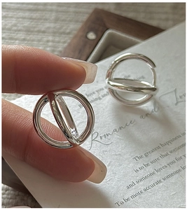 Detail of silver S925 geometric hollow hoop earrings held by hand on a white card background