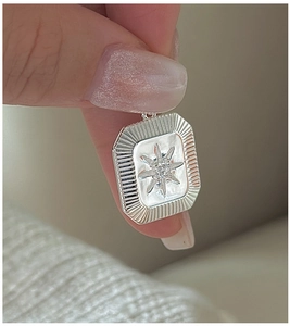 Macro shot of silver square pendant with starburst engraving and centered rhinestone detail