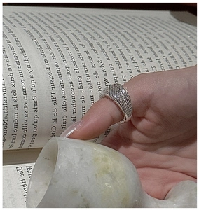 Close-up of S925 silver ring with woven texture on index finger over vintage books