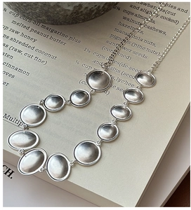 Detailed close-up of matte S925 silver oval disc necklace on minimalist paper background