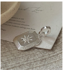 Macro view of S925 silver starburst charm with zircon inlay on a textured fabric