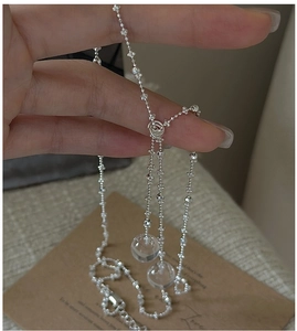 Detail of silver long chain featuring two clear crystal spheres held in hand
