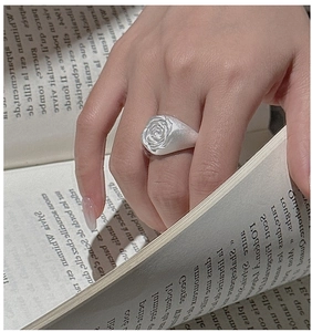 Macro detail of retro white rose seal ring worn on hand with vintage book background