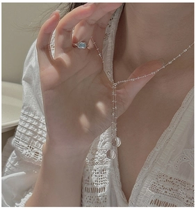 Detailed view of silver Y-necklace with crystal pendants and gemstone ring on a model