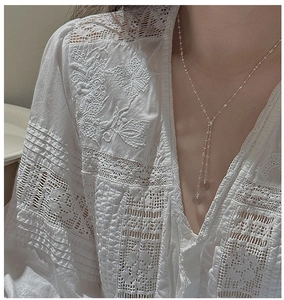 Detail of S925 silver Y-shaped necklace with white crystals on a white lace shirt