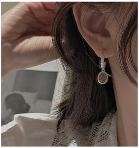 Close-up of S925 silver twist hoop earrings with vintage coin pendant worn by a model