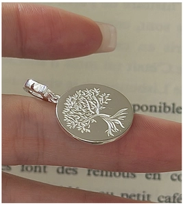 Detailed view of S925 sterling silver Tree of Life pendant held by hand over book pages