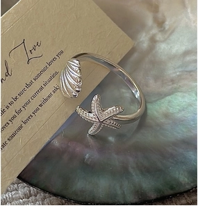 Detailed view of silver starfish and seashell ring inside a shimmering pearl shell