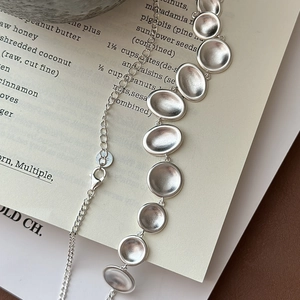 Artistic S925 sterling silver necklace featuring matte oval discs on an open book