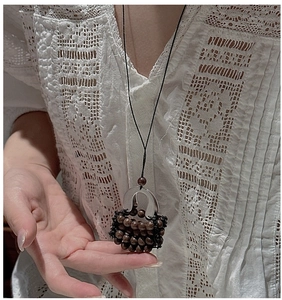Macro view of woven basket pendant with dark wood beads and silver metal on sweater chain