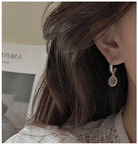 Close-up of S925 silver twist hoop earring with vintage coin pendant on female model