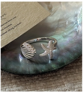 Detailed close-up of a silver starfish and seashell open ring on a pearl background