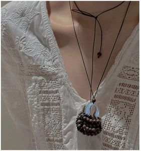 Macro shot of retro wooden bead woven handbag pendant on black adjustable rope chain