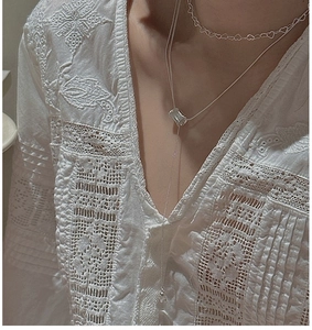 Collier en argent superposé avec pendentif cœur sur chemise en dentelle brodée blanc