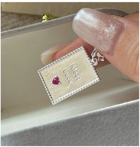 Macro shot of silver rectangular pendant with Meet Luck engraving and heart ruby stone