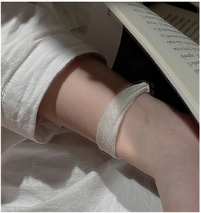 Macro detail of silver mesh weave bracelet paired with white shirt and French book