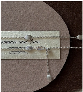 Detailed macro view of silver brushed oval pendants and a lobster clasp on the necklace
