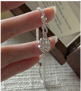 Macro detail of a sparkling silver four-leaf clover pendant bracelet with a beaded chain