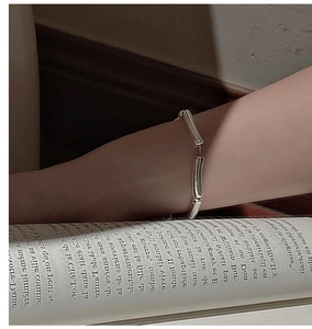 Detail of a minimalist silver hollow tube bracelet worn on wrist over a vintage book