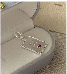 Macro detail of silver rectangular pendant with Meet Luck engraving and red heart zircon