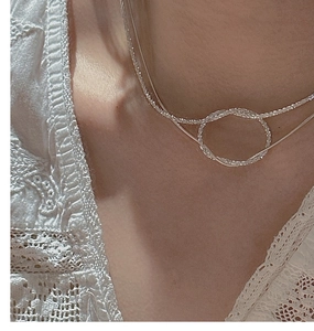 Detail of layered S925 silver necklace with minimalist twisted ring pendant on model