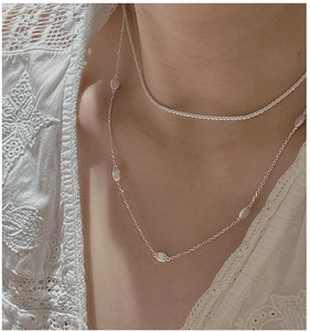 Detail of layered S925 sterling silver necklaces with oval pendant on a model