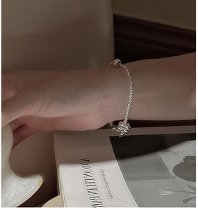 Detail of silver clover bracelet and round bead pendant worn on model wrist