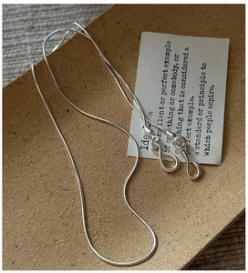 Detail of S925 sterling silver chain with S-hook clasp and infinity charm on brown tray
