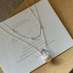 Double layered S925 silver necklace with brushed metal pendant on a vintage paper background
