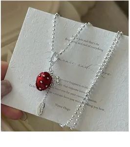 Macro shot of S925 silver beaded chain with red strawberry pendant and oval logo tag