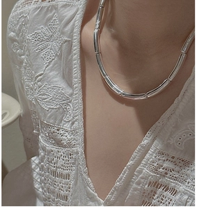 Close-up of minimalist silver tube link necklace on a model with white lace outfit