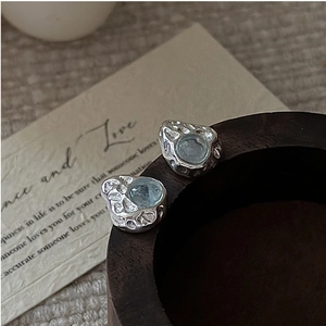Detail of S925 silver stud earrings with hammered texture and light blue gemstone on wood